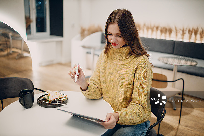 漂亮的年轻女子在咖啡桌上用电子平板电脑喝咖啡图片素材