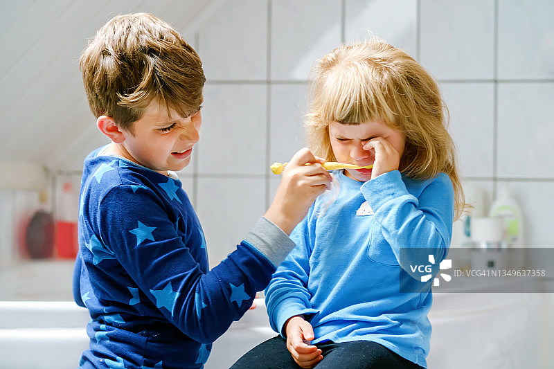 一个学前班的小女孩和一个十几岁的小男孩正在刷牙。哥哥在教妹妹刷牙。伤心难过哭泣的孩子。两个孩子和早上的牙科例行公事。家庭室内。图片素材