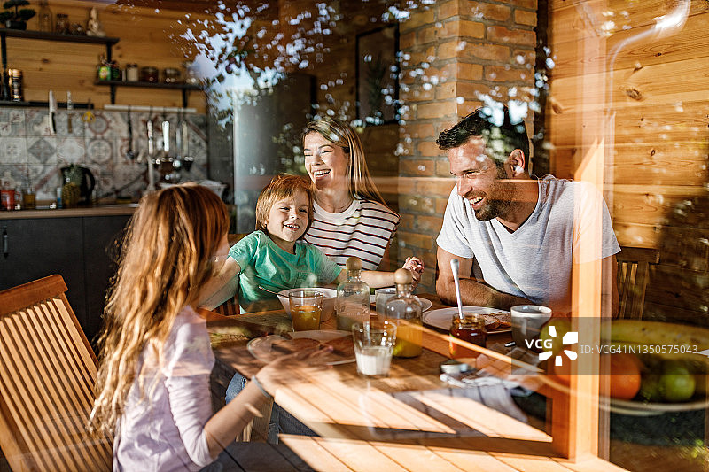 年轻幸福的一家人在餐桌上谈论早餐。图片素材