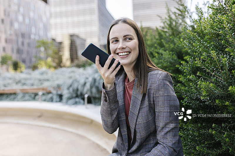 一位时尚的商务女性微笑着用她的手机发送语音信息。图片素材