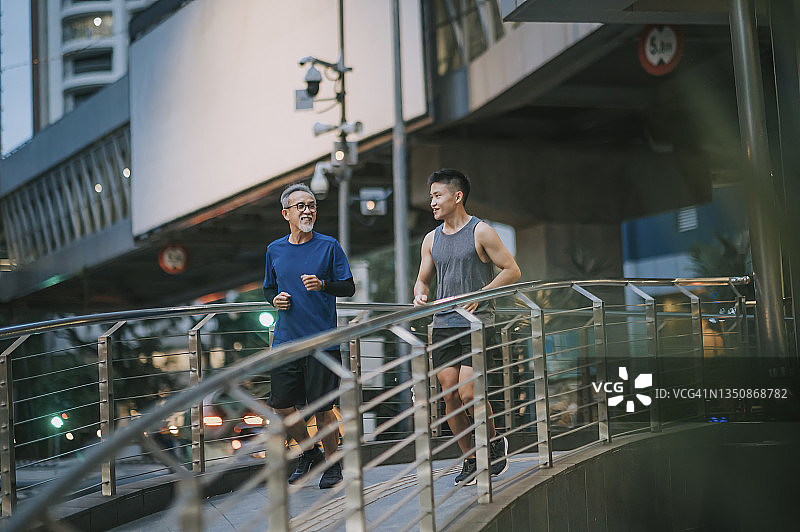 亚洲华人活跃的老人和儿子晚上下班后一起在城里跑步慢跑图片素材