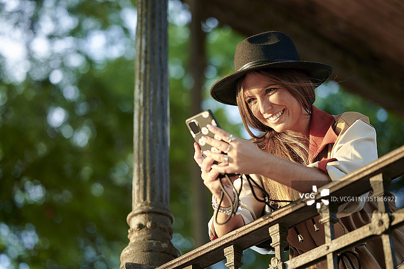 倚在栏杆上用智能手机的微笑女人图片素材