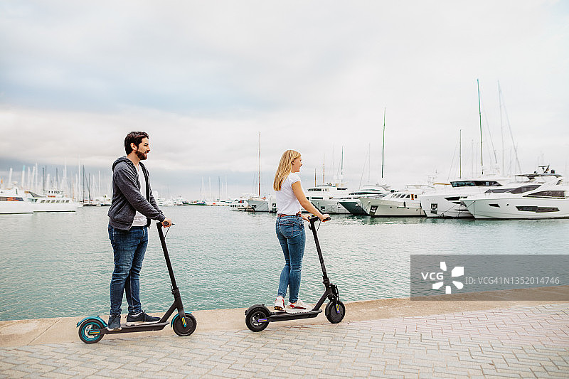 年轻夫妇在港口使用电动滑板车以生态方式移动车辆图片素材