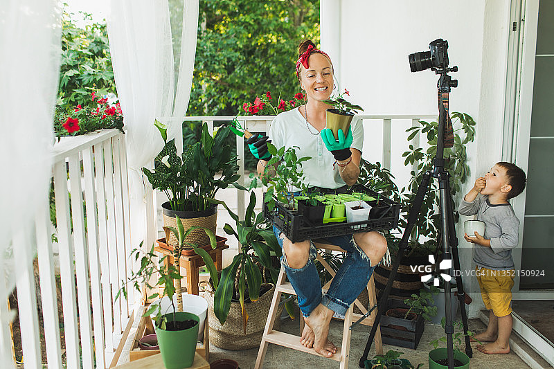 快乐的女人在绿色橡胶手套与盆栽记录园艺教育视频教程在现代lhome露台。图片素材