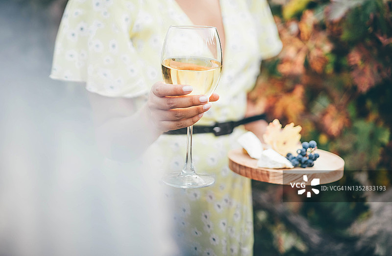在葡萄园里放松的女人。一个女人站着，手里拿着一杯白葡萄酒。图片素材