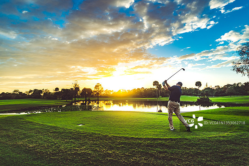 一名男子在风景优美的日落高尔夫球场上挥动高尔夫球棒图片素材
