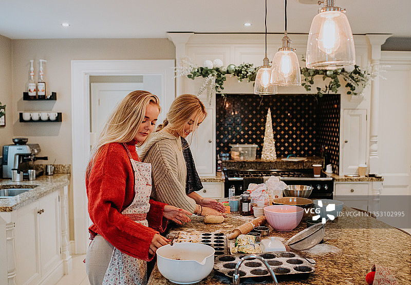 在圣诞节的场景中，两个年轻的女人在厨房里烤碎馅饼图片素材