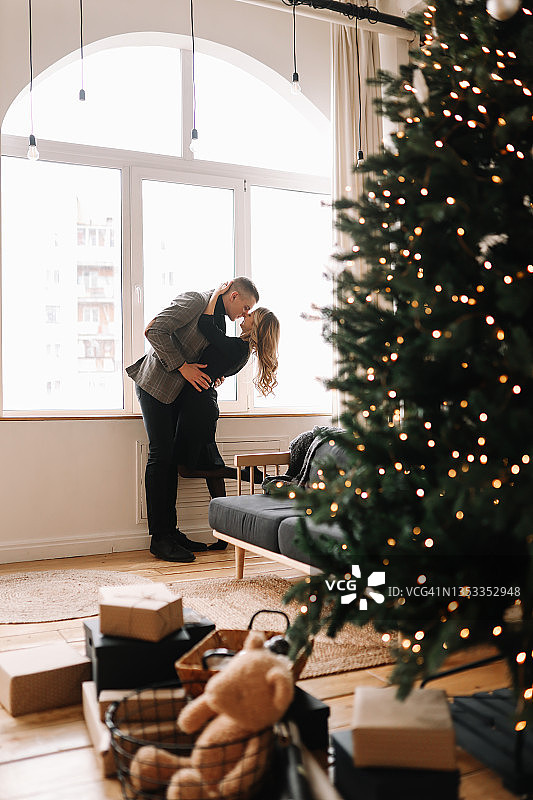一男一女，穿着优雅的衣服，在家里一个舒适的客厅装饰室内，在窗户的背景下，拿着玻璃杯共度圣诞假期图片素材