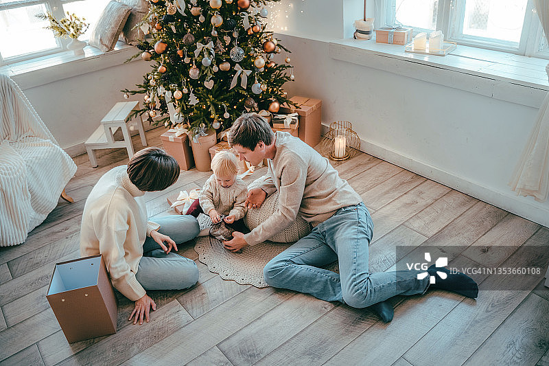 年轻的家庭和一个孩子在圣诞树下打开礼物图片素材