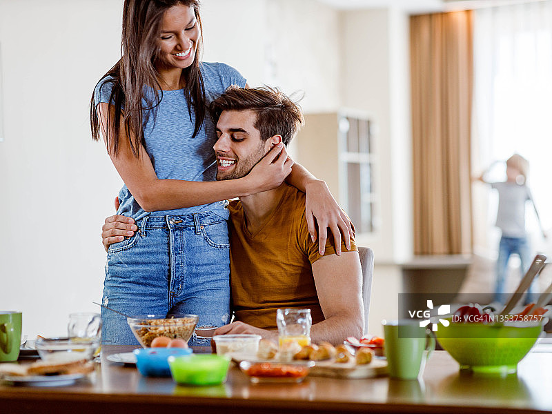 幸福的情侣在早餐时间在餐桌上拥抱。图片素材