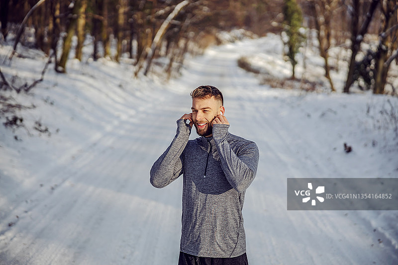 在雪天，快乐的运动员戴着耳机，站在大自然中听着音乐。科技，冬季健身，健康生活图片素材