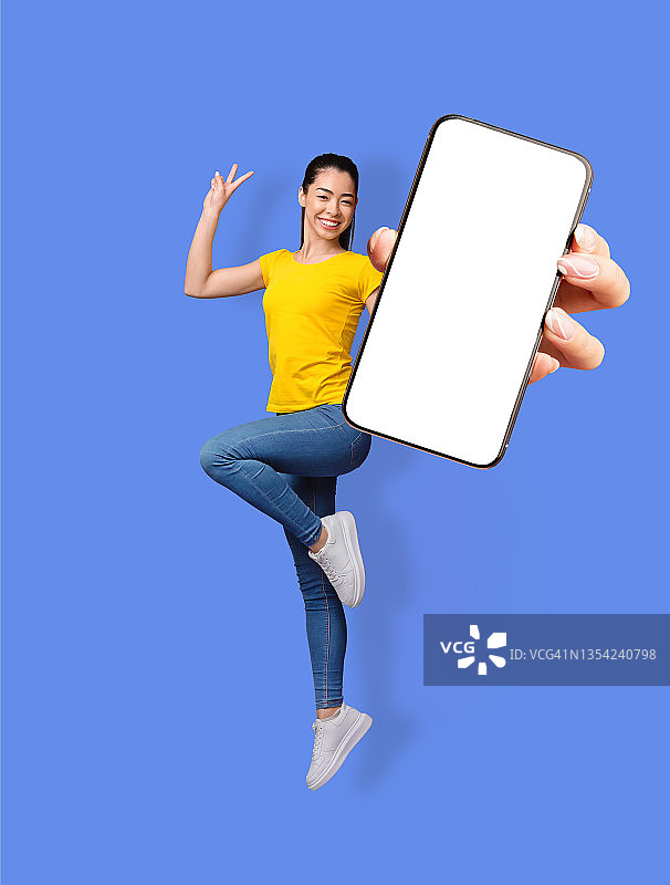 全长度的微笑的年轻亚洲女人跳，手势和平和显示手机与空屏幕，模型图片素材