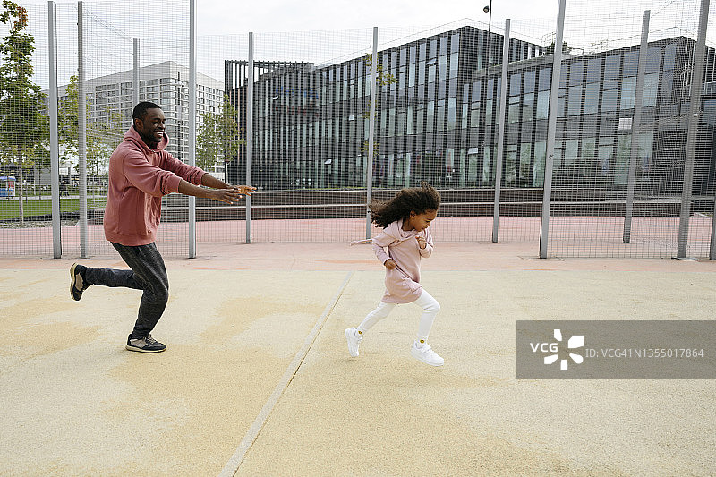 微笑的父亲在运动场上追着女儿图片素材