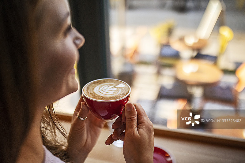 微笑的年轻女子喝着咖啡，看着窗外图片素材