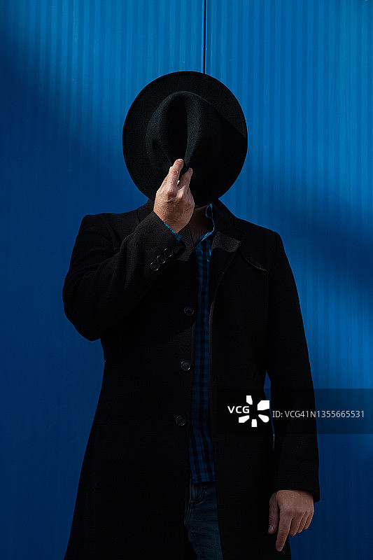 时尚的男人用帽子遮住脸在蓝色的背景图片素材