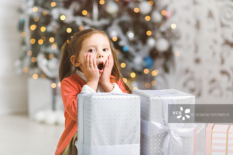 可爱的小女孩惊讶于丰富的圣诞礼物在圣诞树在舒适的房间图片素材