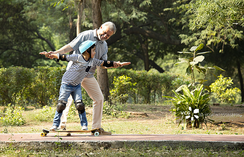 穿着保护性运动服的男孩和爷爷在公园学习滑板图片素材