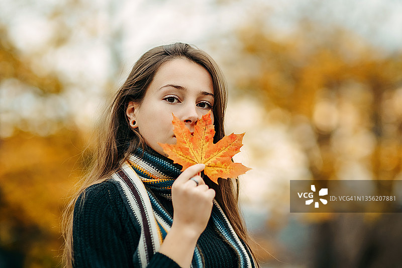 一个快乐的年轻美丽的女人的肖像覆盖她的脸与秋天的叶子图片素材