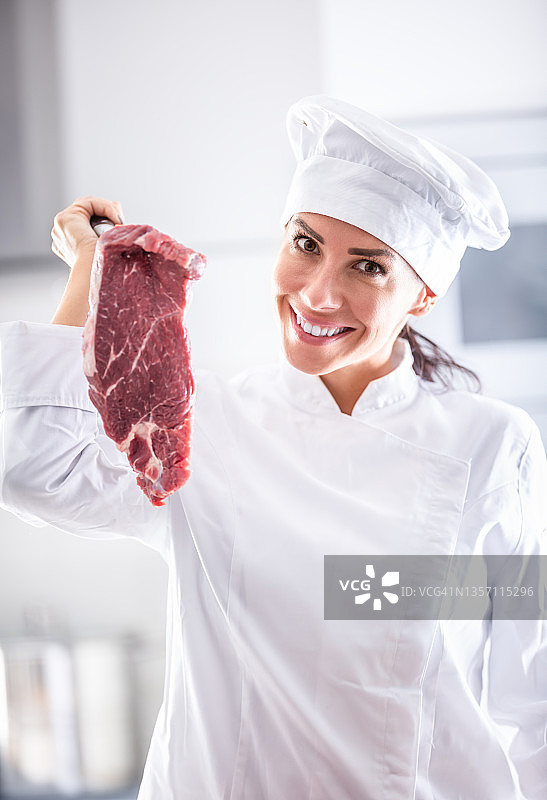 穿着职业装的女厨师手里拿着一大块红肉，面带微笑。图片素材