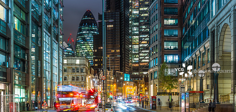 伦敦红色巴士呼啸穿过城市摩天大楼夜间街道全景图片素材