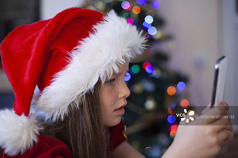 女孩在圣诞帽与圣诞礼物-智能手机图片素材