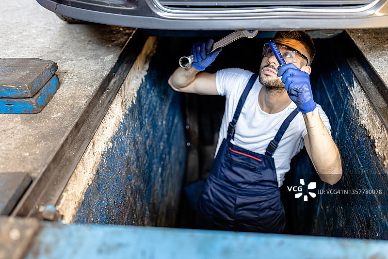 一个男性汽车维修工人正在修理汽车的排气系统。图片素材