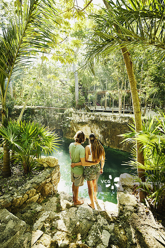 在丛林生态度假胜地放松时，拥抱的夫妇看着天然井的广角后视图图片素材