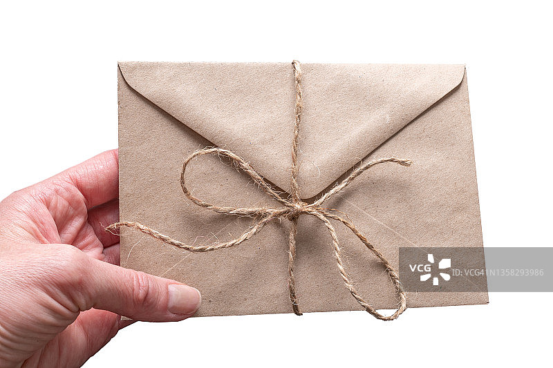 手拿着封闭的棕色工艺信封用麻绳绑在白色的背景孤立。一个祝贺你的信封。图片素材