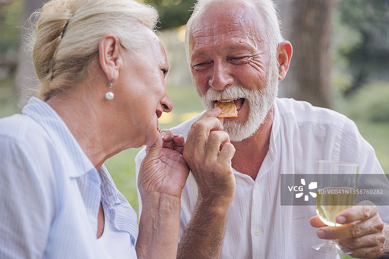 成熟的夫妇在野餐时吃着饼干，喝着白葡萄酒图片素材