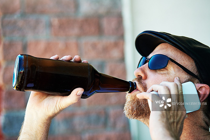 一个成熟的男人一边喝啤酒一边用智能手机图片素材