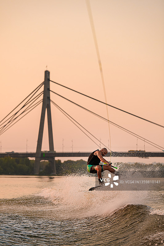 在城市桥梁的背景上，能源人在尾浪板上握着绳子，熟练地跳跃。图片素材