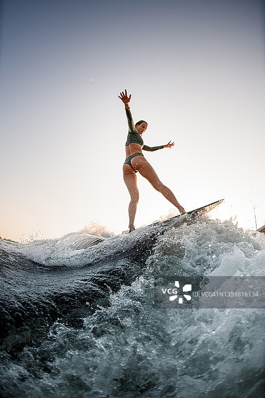 迷人的湿女人在板上冲浪，河上的波浪对着蓝天图片素材