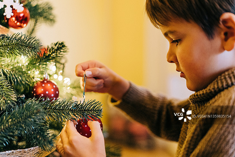 可爱的小男孩在装饰圣诞树。图片素材
