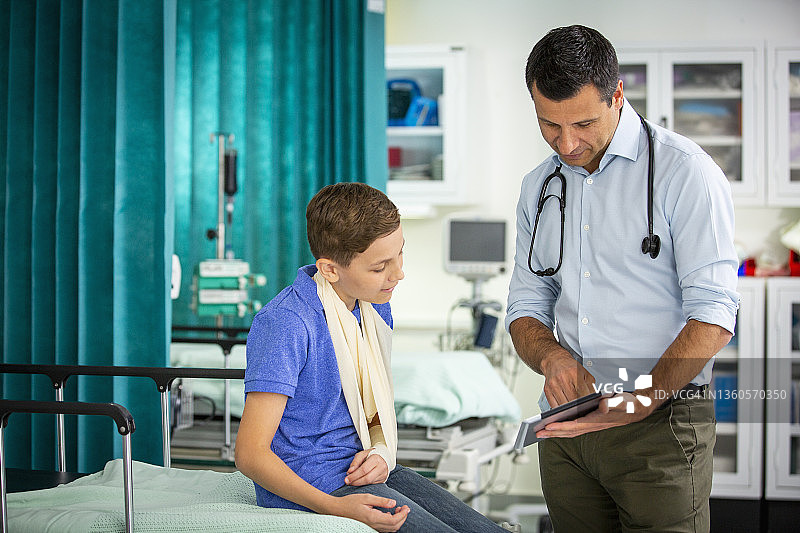 男性儿科医生向手臂吊着绷带的男孩病人展示数字平板电脑图片素材
