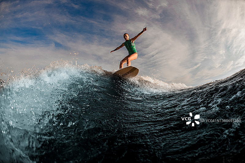 穿着绿松石背心的女子水上冲浪运动员在水上冲浪板上积极地保持平衡图片素材