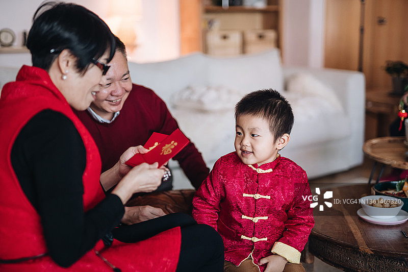 可爱的小孙子穿着传统的红色中国服装，在春节快乐地向爷爷奶奶问候，领取红包(来喜)图片素材