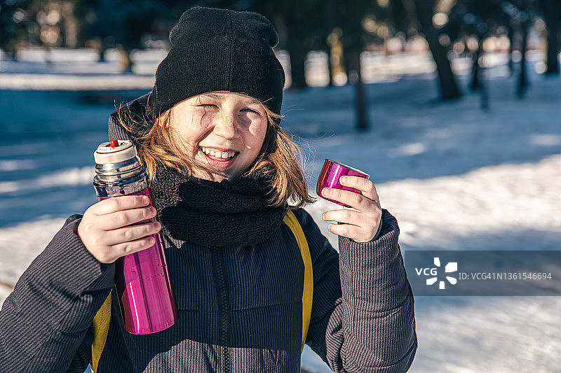 一个小女孩在寒冷的冬天拿着保温瓶站在外面。图片素材