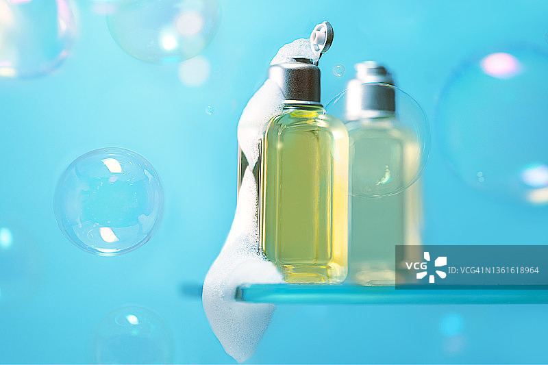 美容产品泡沫肥皂，沐浴露或洗发水和飞行的肥皂泡沫在流行的蓝色背景。图片素材