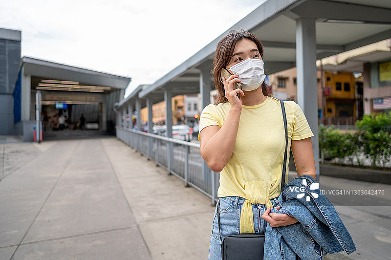 年轻的亚洲女性戴着防护口罩在城市街道上使用智能手机图片素材