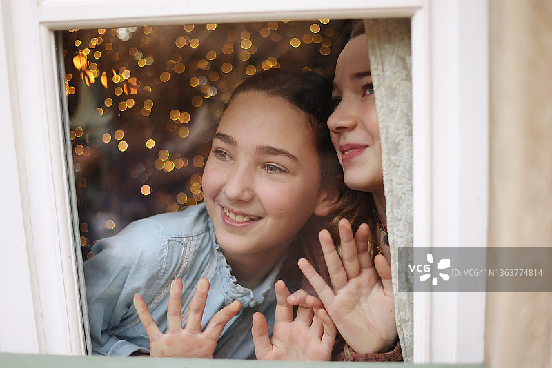 两姐妹透过窗户看着圣诞节的心情图片素材
