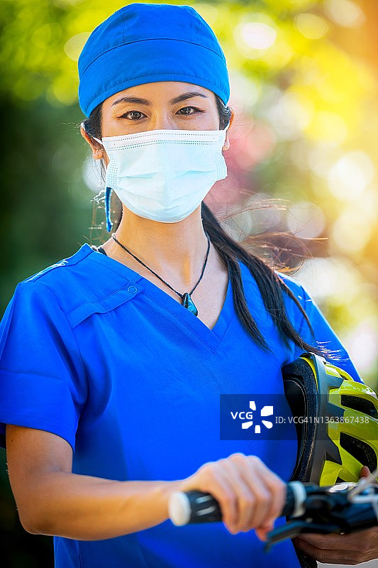 微笑的亚洲女性保健工作者看着相机摆姿势，拿着她的自行车图片素材