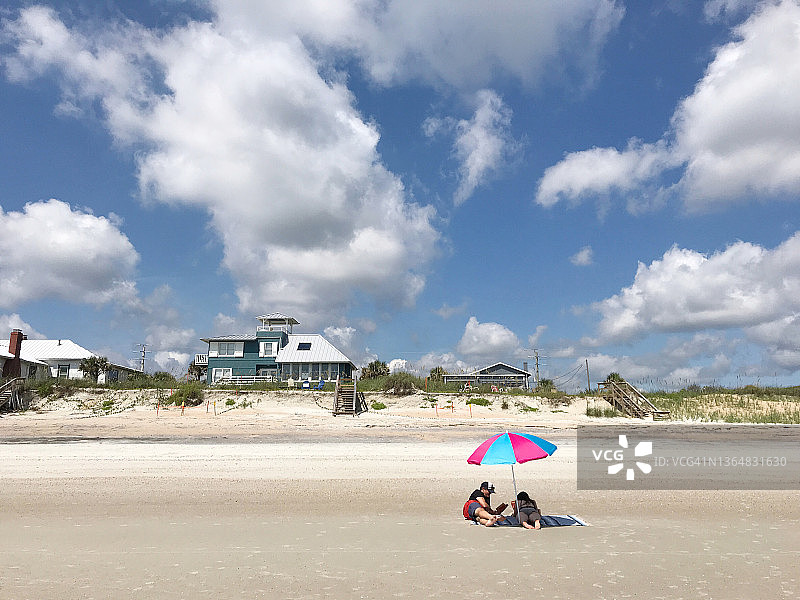 父亲和女儿在沙滩上撑伞休息图片素材