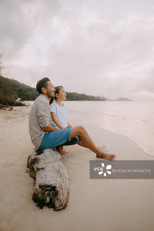 夕阳西下，父亲和小女儿坐在海滩上图片素材