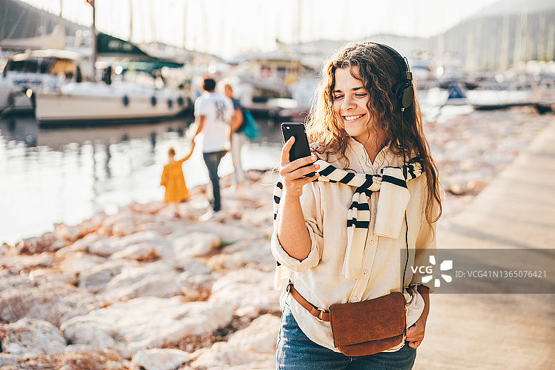 快乐的年轻女子，在海港看着手机。图片素材