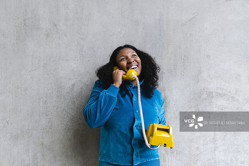 一个快乐的女人在灰色的墙前用复古电话聊天图片素材