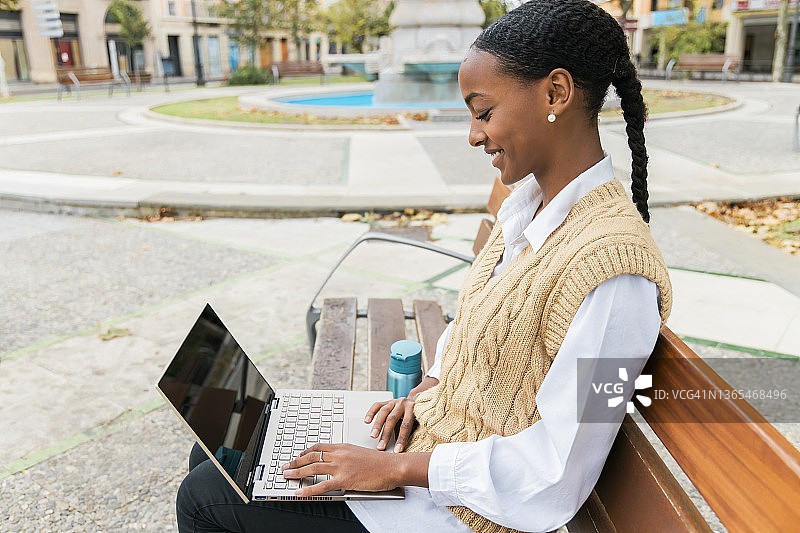 快乐的女孩坐在公园的长椅上用笔记本电脑图片素材