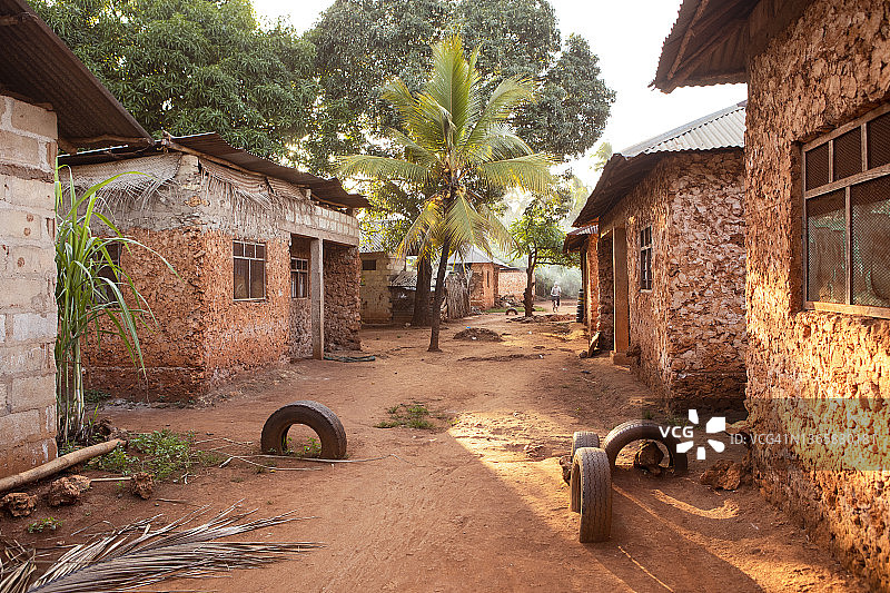 非洲的村庄与棕榈树。灯火通明的街道，生机勃勃的红土和红色的建筑。沿街有棚屋。传统建筑，坦桑尼亚乡村。图片素材