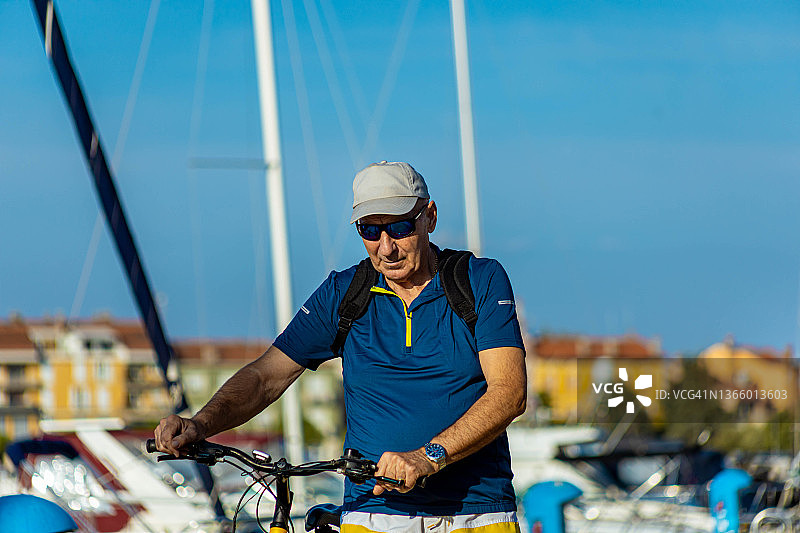 早晨，一些年长的男人在码头边推着自行车，一边观察着停泊在岸边的豪华游艇和帆船图片素材