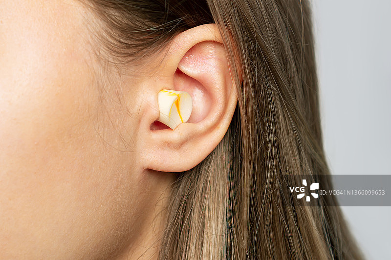 一个年轻金发女人的耳朵与聚氨酯耳塞的特写。防噪音耳机，供睡眠、休息之用图片素材