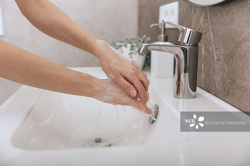 在水龙头下洗手。用肥皂洗手以预防冠状病毒的传播，防止冠状病毒在公共卫生间或公共卫生间的卫生传播。卫生概念手部细节图片素材
